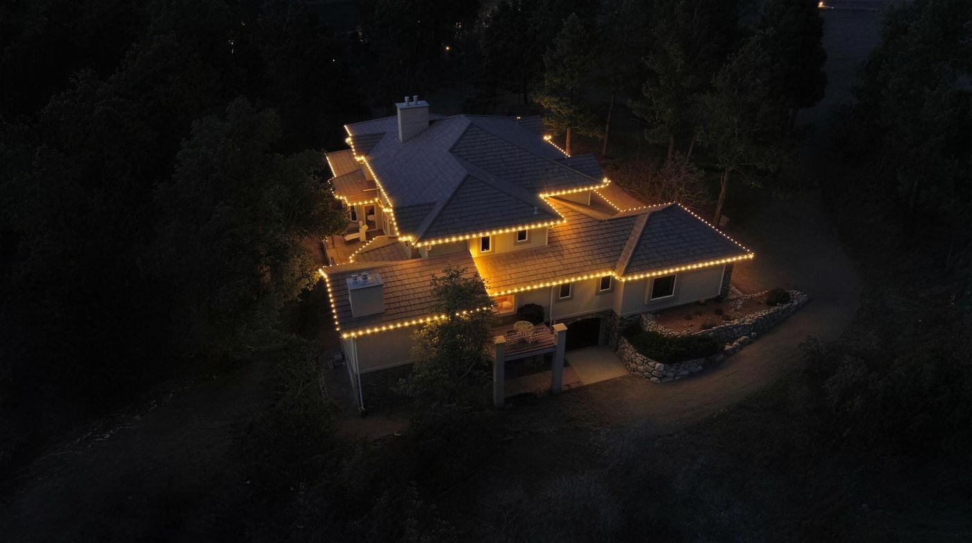 Aerial view of a mountain home among pines with warm roofline lights